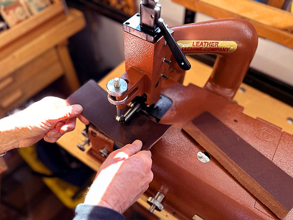Worker feeds a piece of leather through the skiver machine